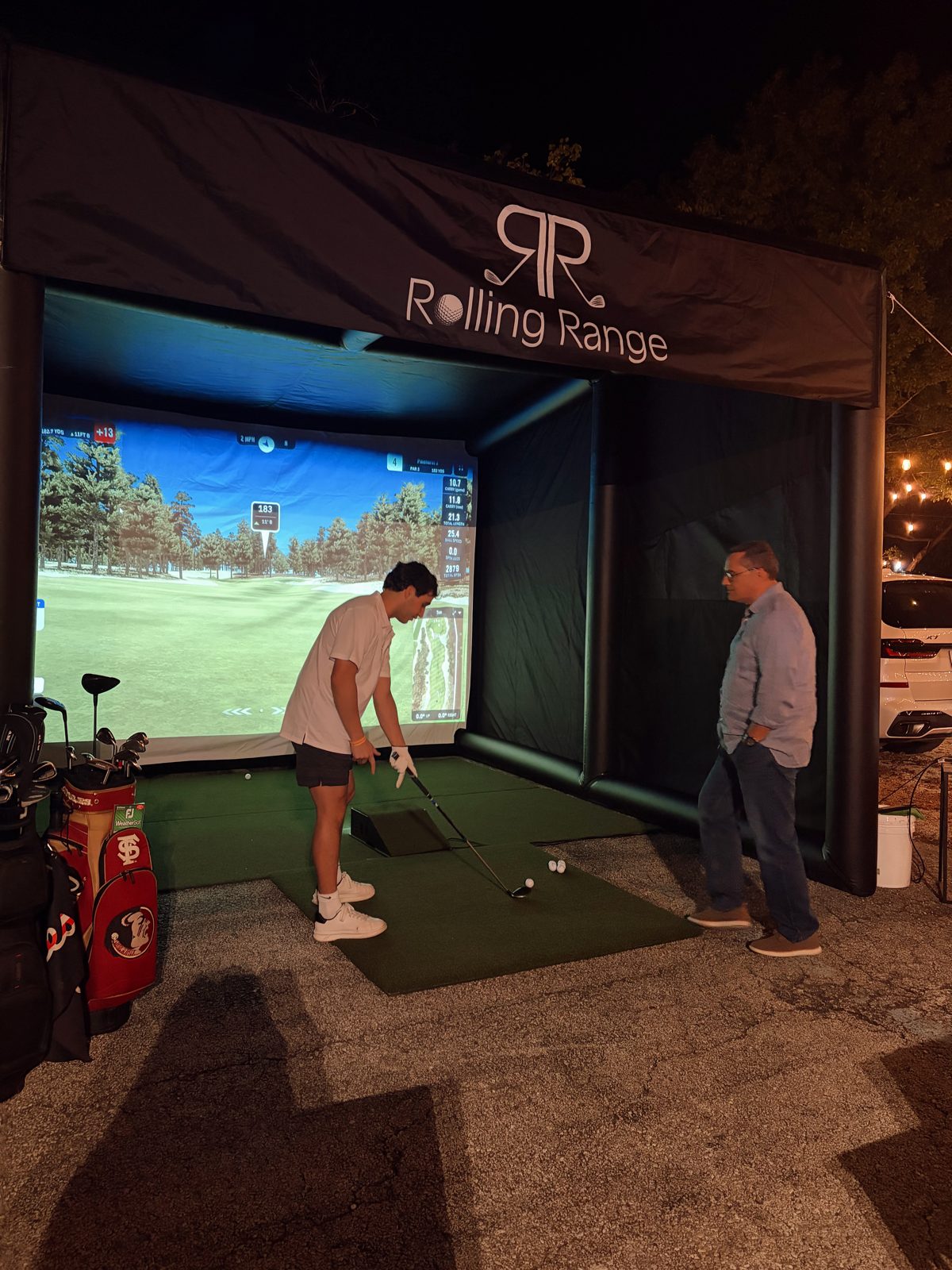 Rolling Range mobile golf simulator enclosure with a guest playing at a night event