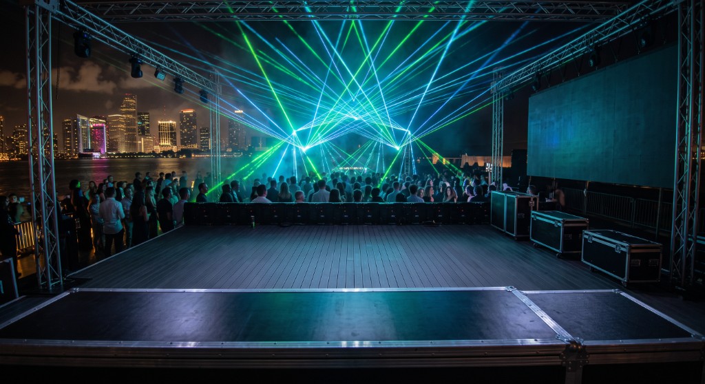 Professional green and cyan laser show beams over a waterfront crowd with city skyline at night
